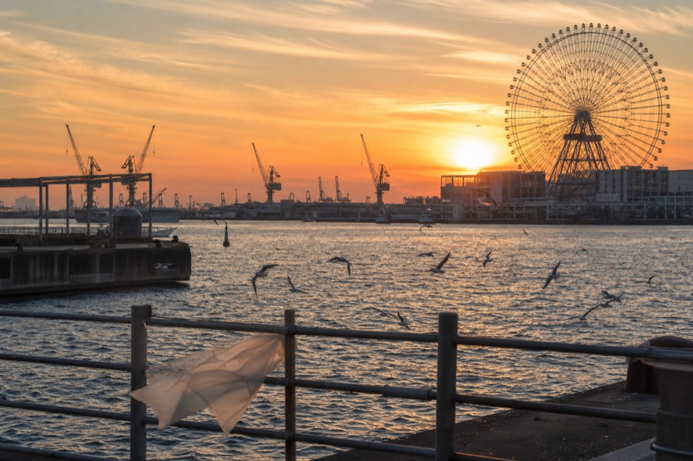 Sunset over Osaka Bay with a large ferris wheel silhouetted against an orange sky