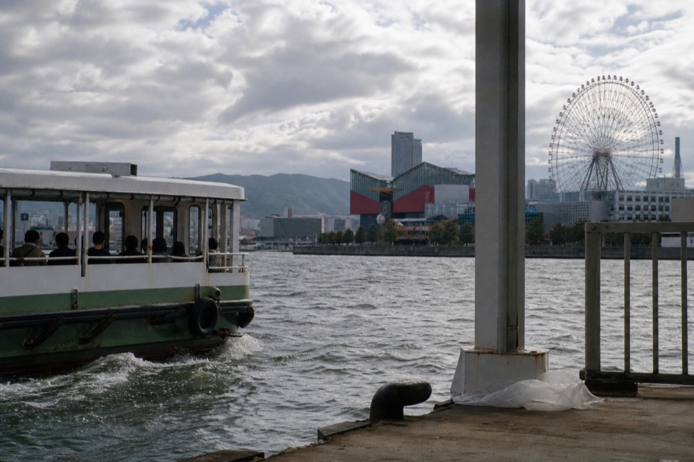 A small shuttle ferry crossing a harbour toward a waterfront pier district