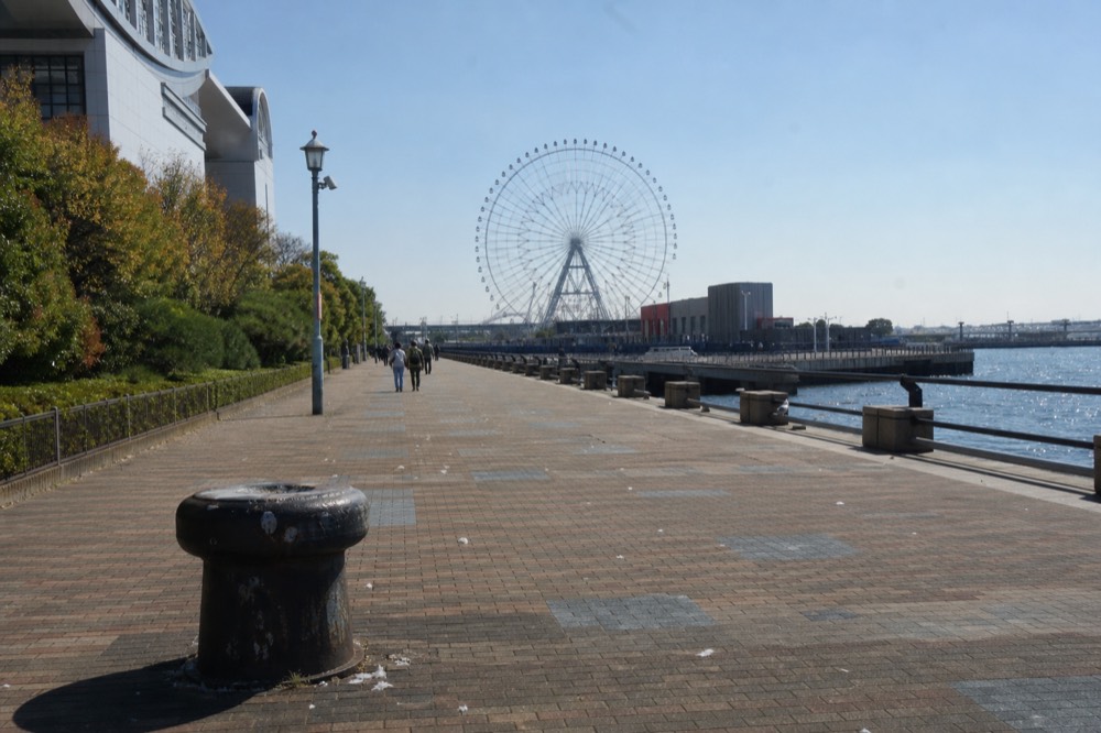 A wide waterfront promenade leading toward a giant Ferris wheel on a clear day