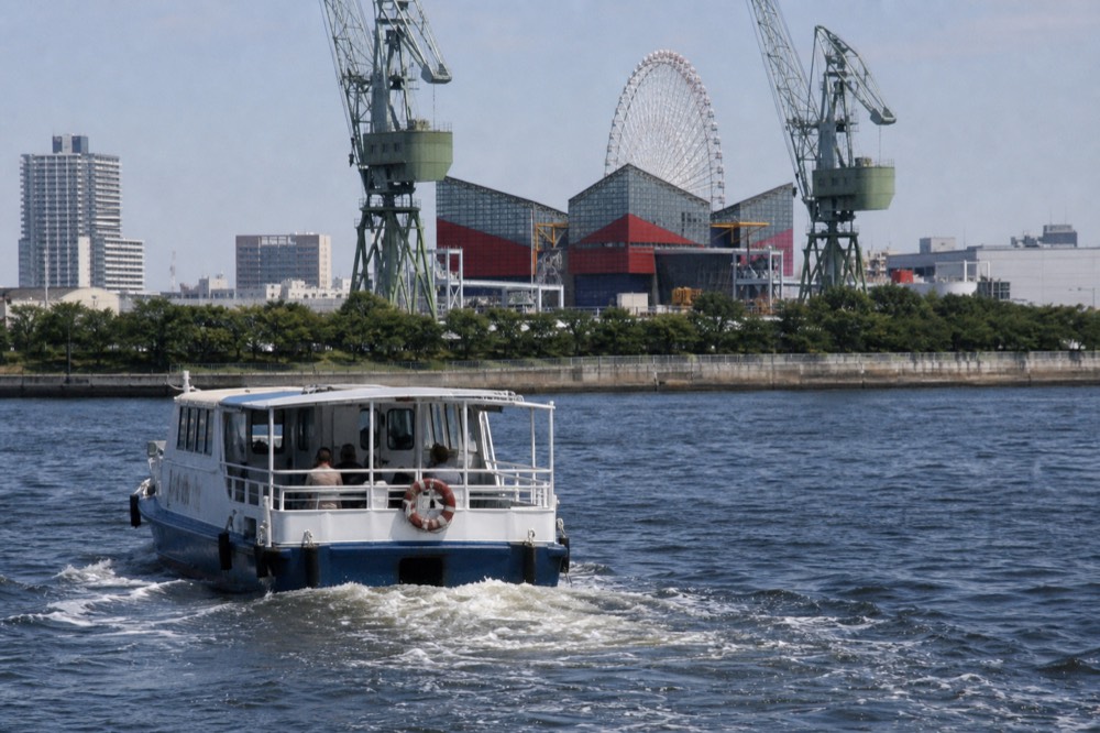 Small shuttle ferry crossing Osaka Bay toward an aquarium building and Ferris wheel