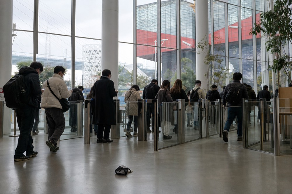 A busy aquarium entrance hall with a ticket gate and visitors holding phones