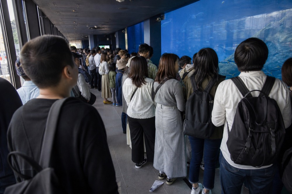 A crowd of visitors filling a walkway in front of a tall glass aquarium wall