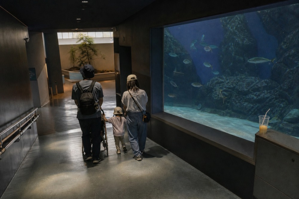 A family walking down a wide sloping aquarium corridor past a large tank