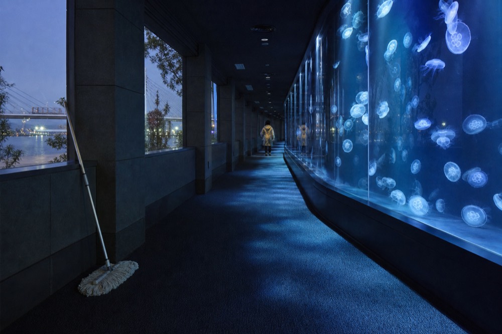 A quiet aquarium corridor curving past a glass wall of drifting jellyfish