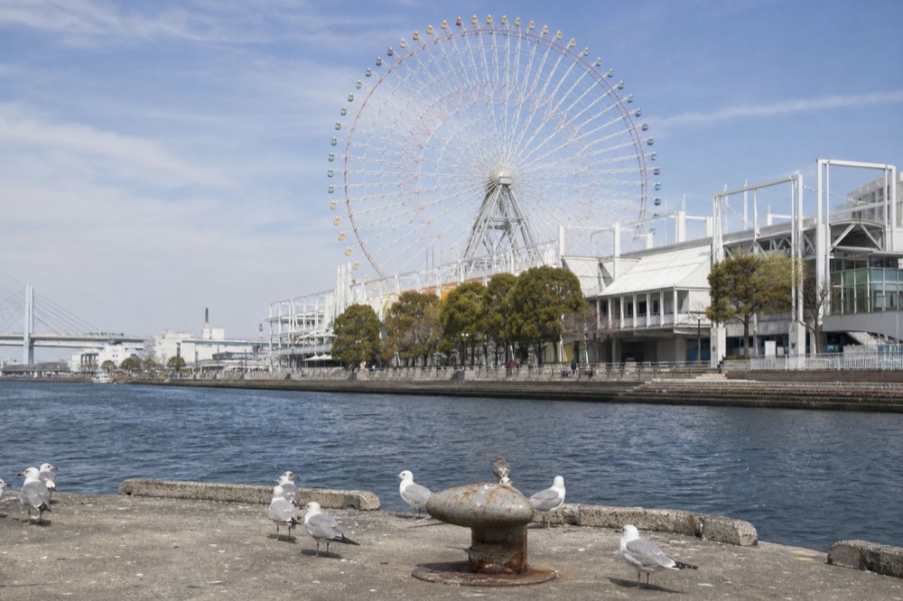 Large Ferris wheel standing above a waterfront mall complex in daylight