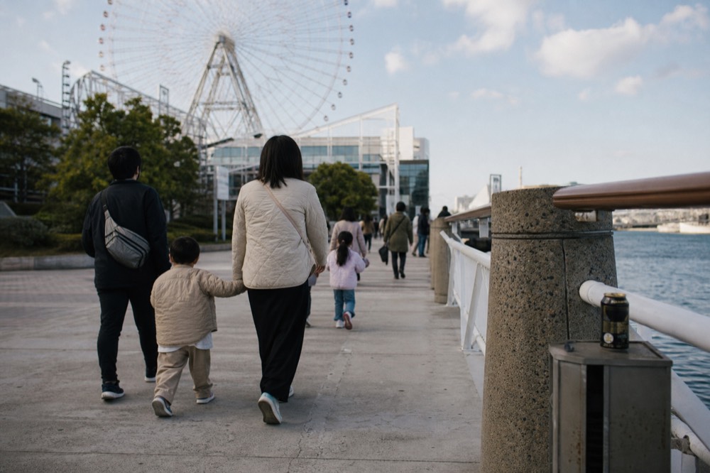 Families walking along a waterfront promenade beside a large observation wheel