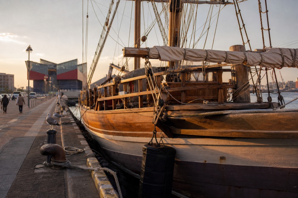 A replica wooden sailing ship moored at a harbor wharf