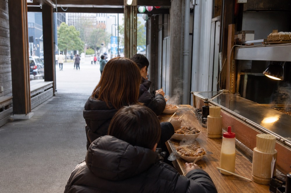 Family eating at a counter in a food alley beside a large aquarium building